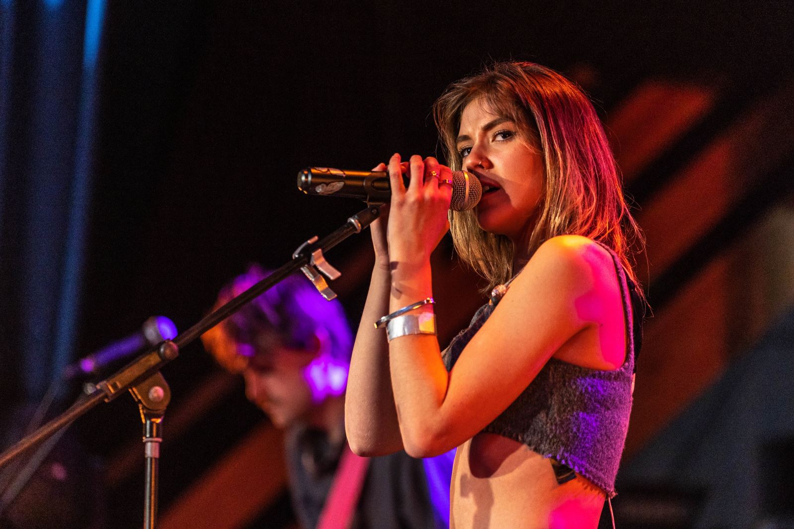 A female singer on stage with a microphone pressed to her mouth and her eyes looking at the camera