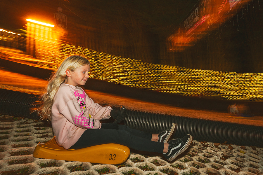 A child speeds downhill on a floodlit toboggan run