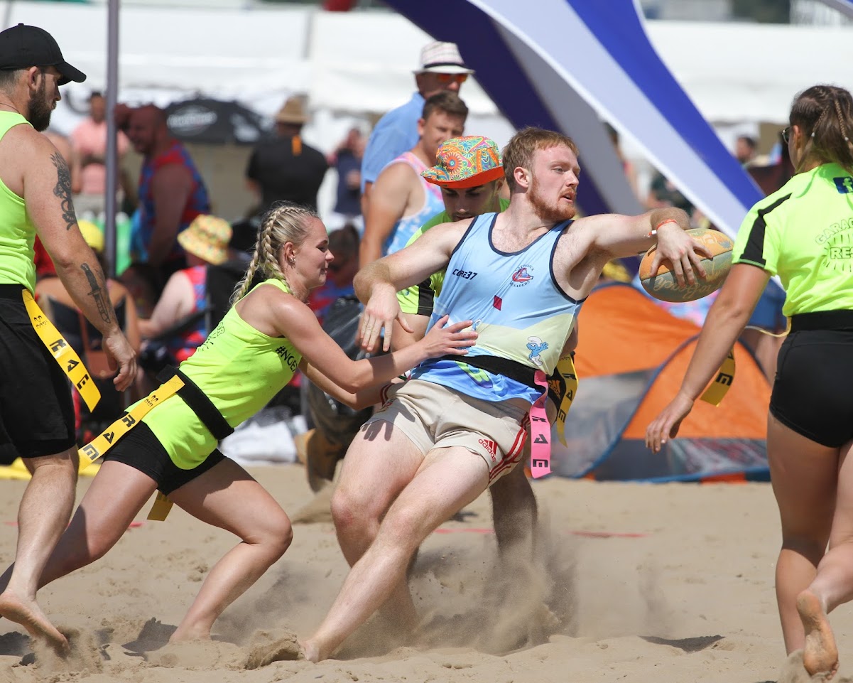 A beach rugby player offloads the ball as he's tackled by a female beach rugby player