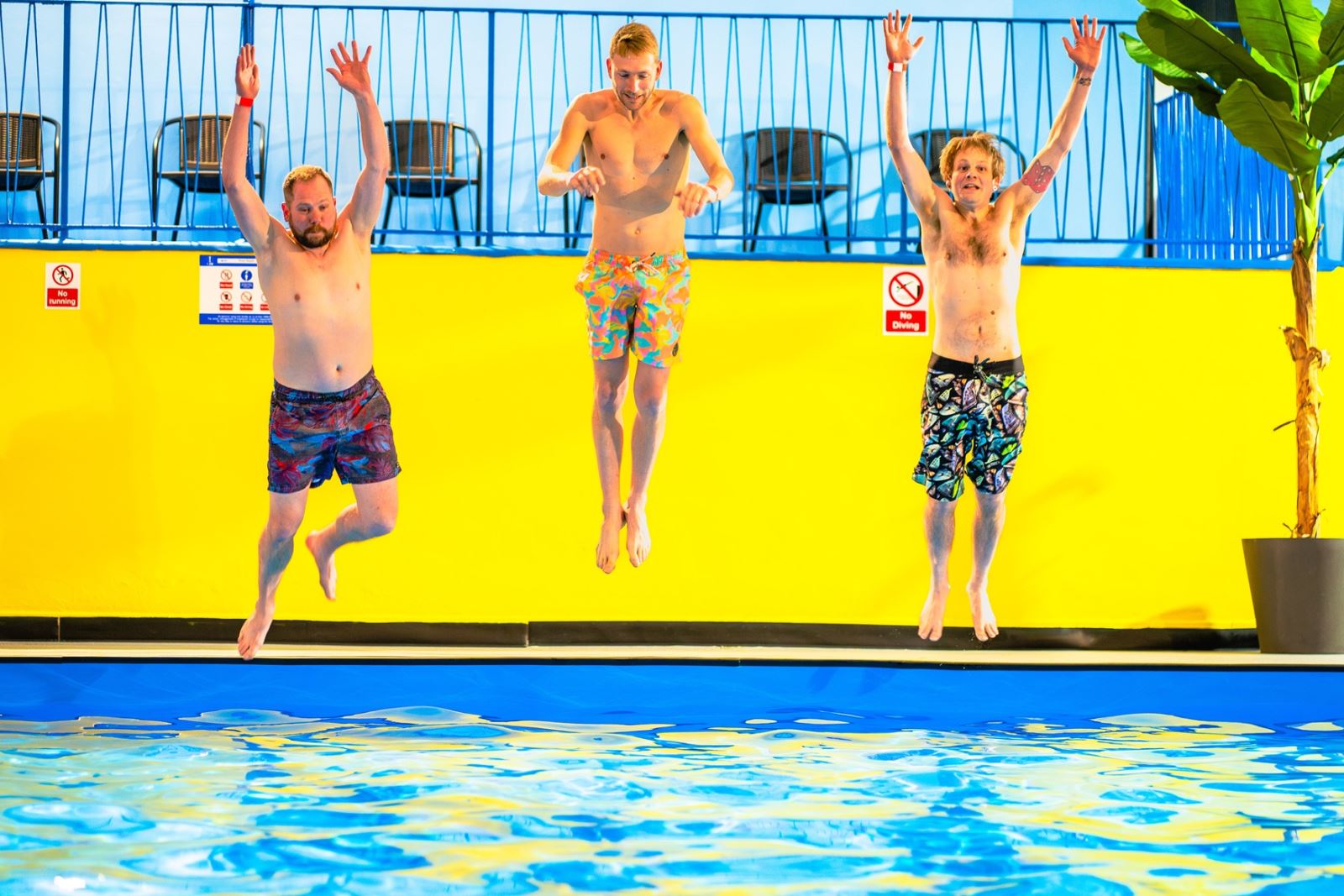Three men in swimming shorts jumping into a swimming pool
