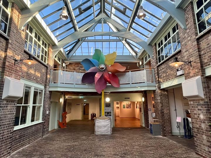 The interior courtyard of Weston Museum featuring Banksy's pinwheel sculpture, set under a glass ceiling with exposed brick walls.
